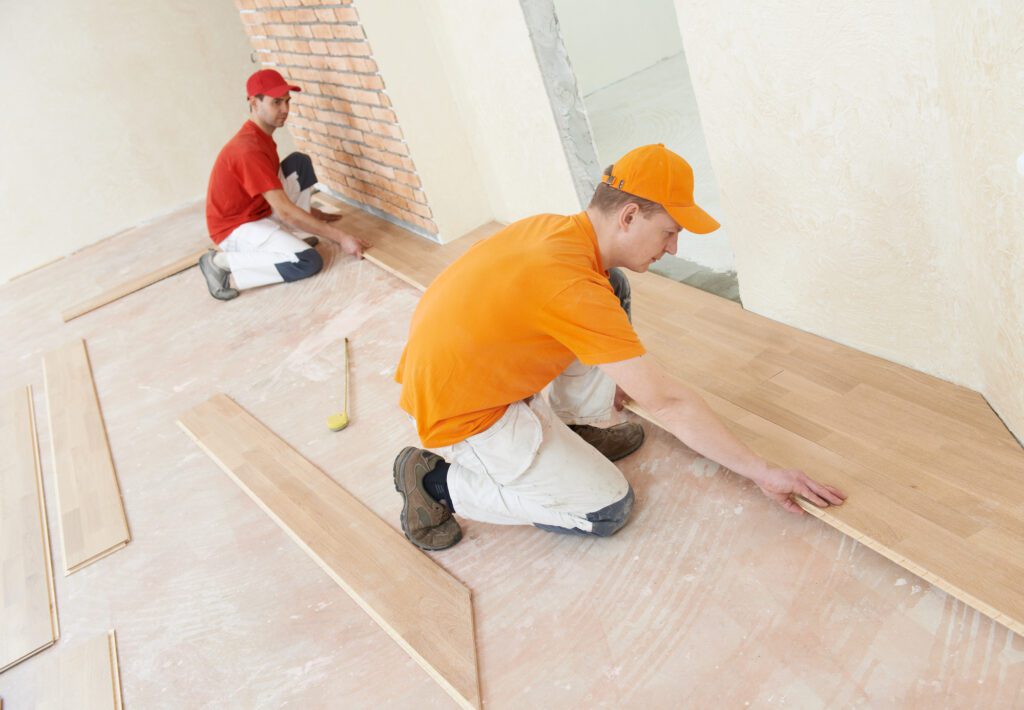 Two parquet carpenter workers installing wood board during flooring work