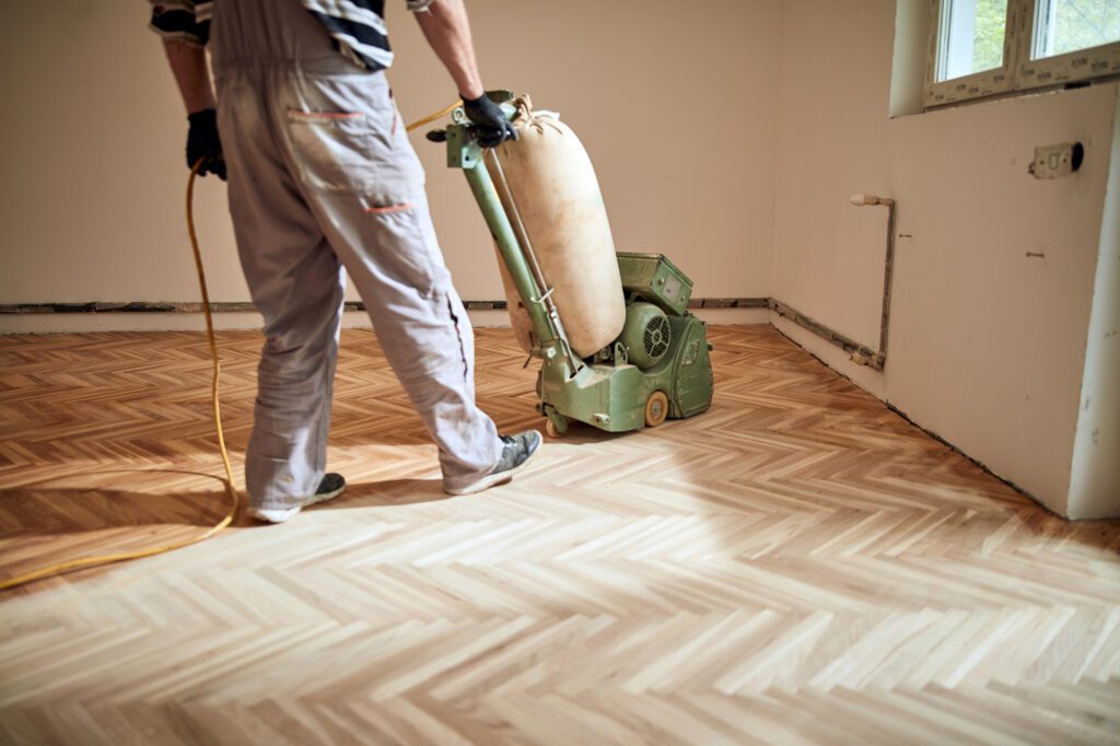 Repairman restoring parquet with a sanding machine.